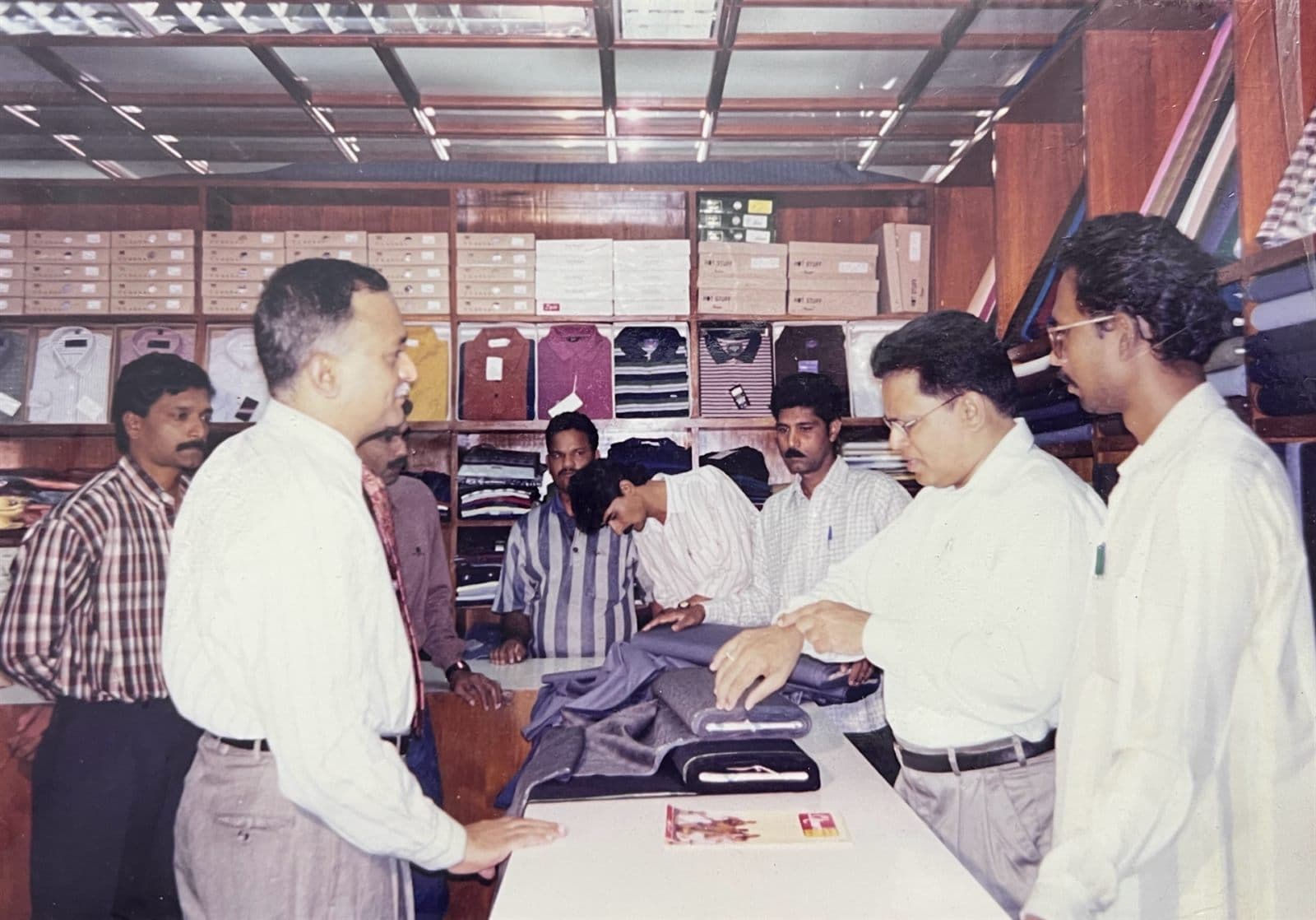 Chairman M.A.A.K.’s Personal Salesmanship & Client Advisory (2000s) - Chairman Mohammed Ahmed Ali Khan (M.A.A.K.) personally demonstrating suiting cuts, fabric drape, and bespoke tailoring at the counter. | MF.Khan Heritage Archives Visakhapatnam