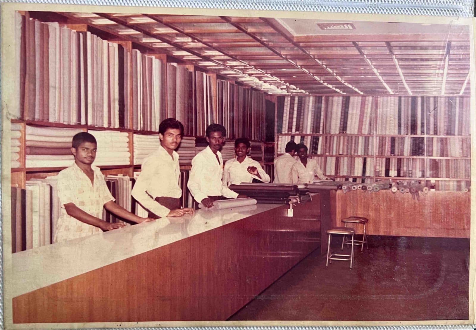 Fabric Showroom & Sales Consultants at the Ready (1980s) - Long wooden fabric display counters stocked with thousands of premium suiting bolts, with attentive sales staff ready to assist bespoke clients. | MF.Khan Heritage Archives Visakhapatnam